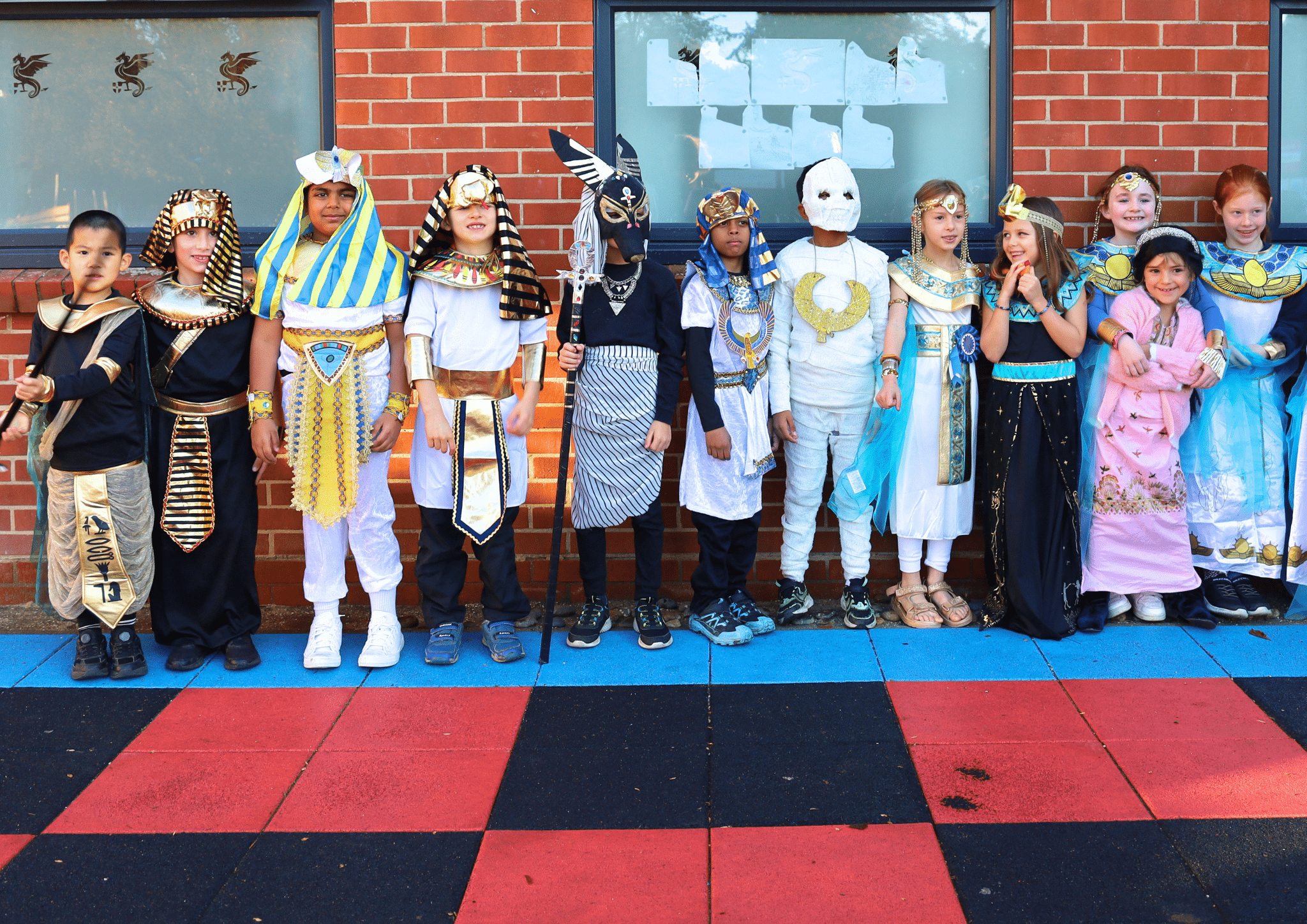A group of children dressed in Ancient Egyptian-themed costumes posing for a photo against a brick wall.